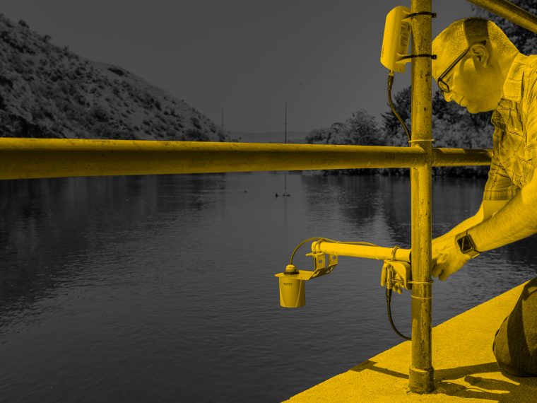 A technician lowering a water-quality sensor into a reservoir from a railed platform.